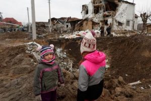Dy fëmijë ukrainas qëndrojnë pranë një vendi që është goditur nga sulmet ruse në periferi të Kievit. /REL