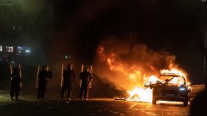 Pjesëtarët e policisë përballen me protestuesit pranë një makine policie të djegur pas një sulmi me thikë në afërsi të një shkolle në Dublin. Irlandë, 23 nëntor 2023.