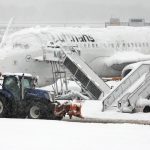 Një automjet gërryes kalon pranë një avioni të mbuluar me borë në aeroportin e Mynihut.