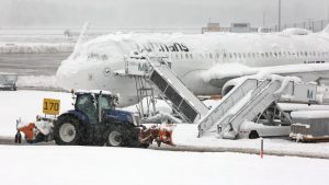 Një automjet gërryes kalon pranë një avioni të mbuluar me borë në aeroportin e Mynihut.