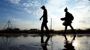 Dy njerëz duke ecur mbi një pellg uji në një rrugë në Afrikën e Jugut, më 26 maj 2023.