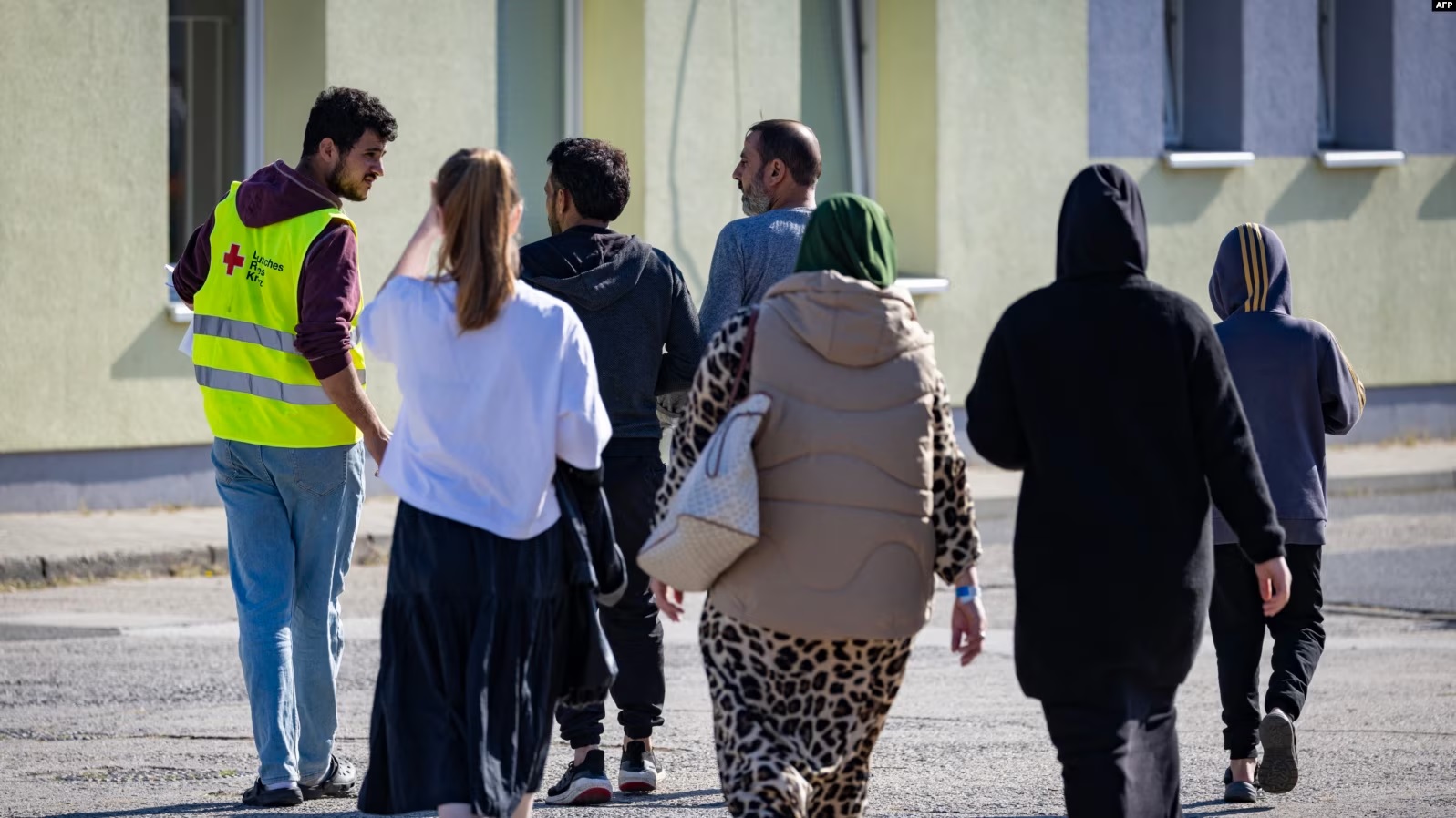 Një vullnetar i Kryqit të Kuq së bashku me një grup azilkërkuesish në një qendër për migrim në Gjermani. Shtator 2023.