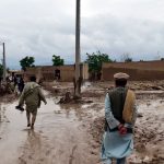 Njerëz shihen në afërsi të shtëpive të dëmtuara nga vërshimet në Afganistan, 11 maj 2024.