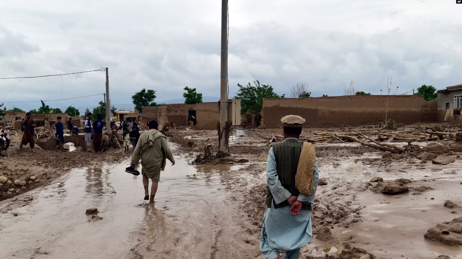 Njerëz shihen në afërsi të shtëpive të dëmtuara nga vërshimet në Afganistan, 11 maj 2024.